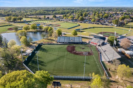 Aerial view of a scenic baseball stadium with lush green field, surrounding trees, and nearby recreational areas.