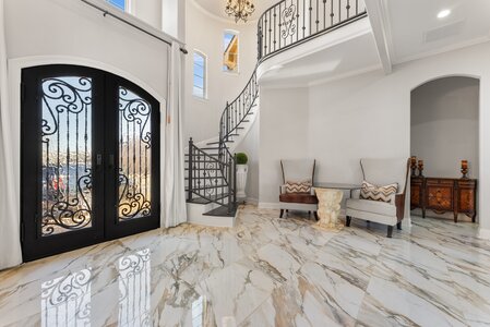 Elegant marble-tiled foyer featuring ornate black iron door and stylish seating area.
