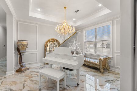 Luxurious white grand piano with crystal chandelier and gold accents in elegant home interior.