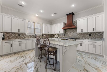 Elegant kitchen design with white cabinets, marble island, and copper range hood.