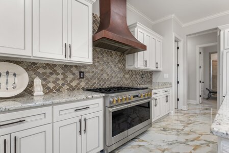 Bright, spacious kitchen featuring white cabinets and a stylish bronze range hood.