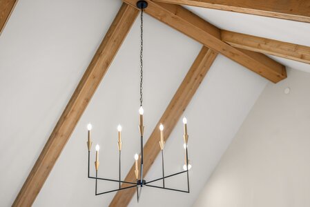 Elegant chandelier with LED bulbs hanging from a chain beneath wooden ceiling beams.