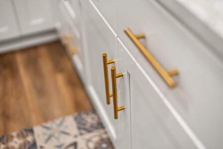 White kitchen cabinets with stylish gold hardware and wooden flooring.