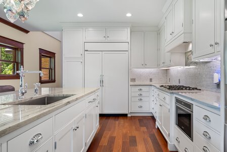 Bright white kitchen with elegant cabinetry and wooden flooring, featuring modern appliances.