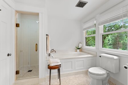 Bright bathroom featuring a walk-in shower, cozy bathtub, and large windows showcasing lush greenery.