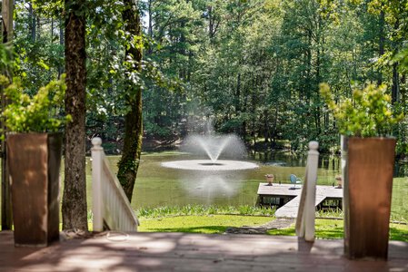Serene lakeside view with a fountain, trees, and a wooden dock, perfect for relaxation and outdoor activities.