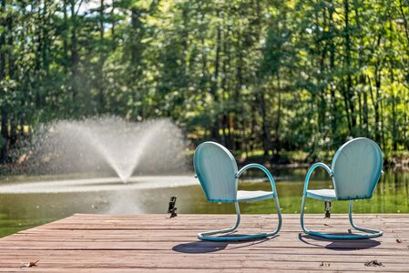 Bright outdoor scene featuring two blue chairs by a peaceful lake.