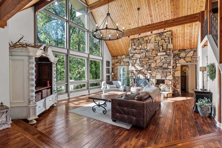 Spacious living room with huge windows, stone fireplace, and rustic wooden interior.