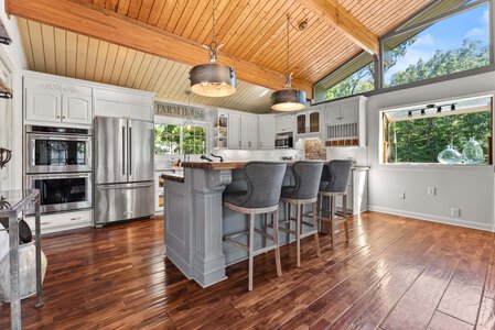 Bright farmhouse kitchen featuring white cabinets, stainless steel appliances, and large windows with a scenic outdoor view.