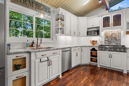 Bright white kitchen with marble countertops, copper accents, and large window view.