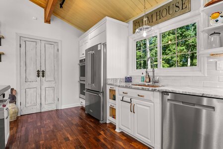 Bright kitchen with stainless steel refrigerator, dishwasher, and white cabinetry under a wooden vaulted ceiling.