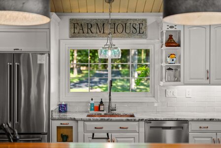 Bright farmhouse kitchen with white cabinetry and hanging light fixture.