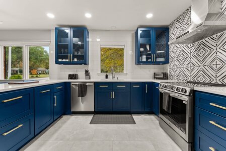 Bright blue kitchen cabinets, stainless steel appliances, and black-and-white geometric backsplash for modern style.