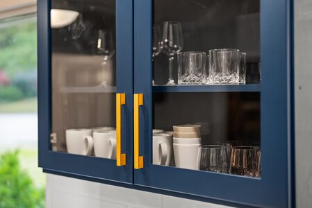 Stylish blue glass kitchen cabinet with glasses and mugs, perfect for modern home kitchen storage.