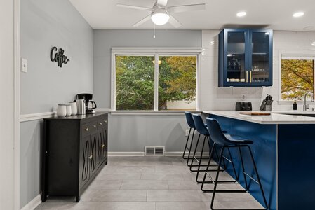Stylish kitchen with blue cabinets, breakfast bar, and large windows overlooking trees.