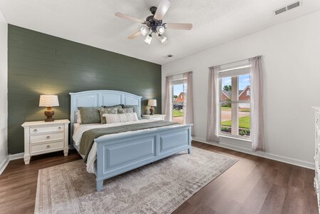 Bright bedroom featuring a green accent wall, cozy bedding, and natural light from large windows.