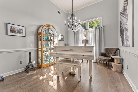 Bright living space featuring a white grand piano, chandelier, and decorative accents with Parisian-themed art and a display cabinet.