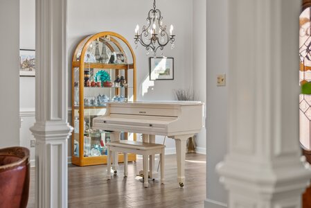 Charming white grand piano in elegant living room with antique chandelier and display cabinet for collectibles.