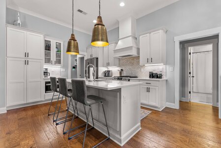 Bright, contemporary kitchen featuring white cabinets, wooden floor, and gold pendant lighting. Perfect for family cooking and entertaining.