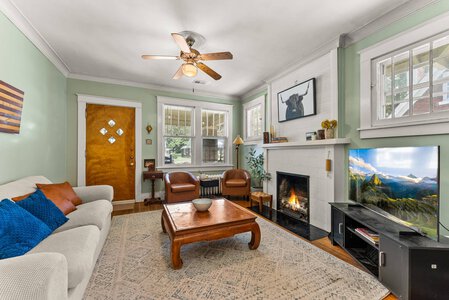 Bright living room featuring a white brick fireplace, large windows, and a flat-screen TV, perfect for relaxing and entertainment.