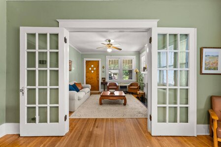 Bright living room with classic style, white wood trim, large windows, and wooden floor. Cozy space with comfortable seating.