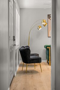 Elegant black velvet chair with gold accents and contemporary arc lamp in stylish living space.