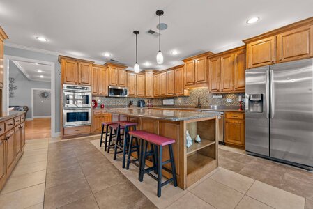 Spacious kitchen featuring warm wooden cabinets, granite countertops, stainless steel refrigerator, and modern lighting fixtures, perfect for family cooking.