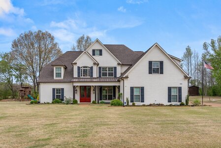 Beautiful white house with black shutters, lush yard, and American flag in a suburban setting.