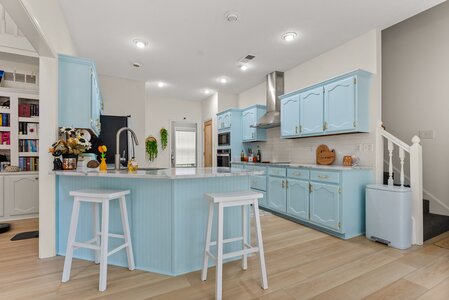 Bright, inviting blue kitchen featuring a breakfast bar, light wood flooring, and modern appliances.