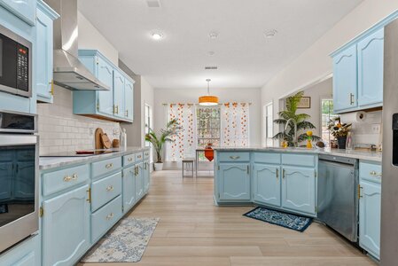 Bright blue kitchen cabinets with gold handles, white countertops, and decorative plants in a spacious, stylish kitchen.