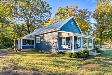 Bright blue house with spacious porch surrounded by fall foliage and trees.