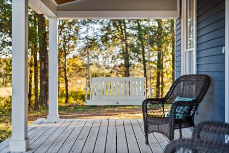 Outdoor porch with swing and wicker chair, perfect for relaxing in nature's beauty.