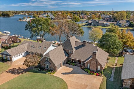 Aerial view of beautiful lakeside house with lush landscaping and surrounding water.