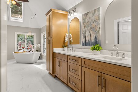 Bright bathroom with wooden vanity, white marble countertop, artwork, and decorative plants.