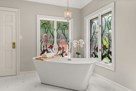 Stunning bathroom featuring a modern white bathtub with decorative stained glass windows of cranes and nature.