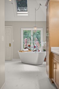 Luxury bathroom with clawfoot tub, stained glass flamingo window, and bright natural light.