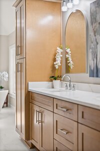 Bright bathroom vanity with wooden cabinetry, orchid plant, and modern mirror.