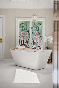 Stylish bathroom with a soaking tub, stained glass flamingo window, and elegant decor.