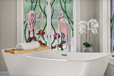 Luxury bathtub with stained glass flamingo design, modern bathroom decor with orchids and towel.