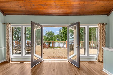 Spacious lake house with open glass doors, inviting outdoor deck, and beautiful water and nature scenery.
