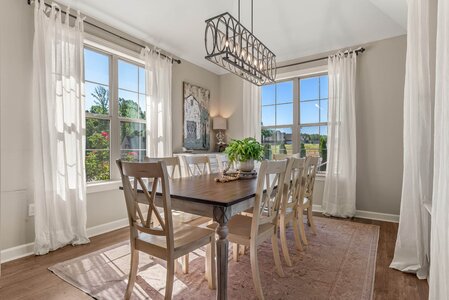 Bright dining area with natural sunlight, overlooking lush greenery through large windows.