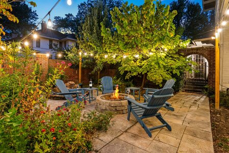 A tranquil outdoor living space featuring a fire pit, garden, and string lights for evening relaxation.