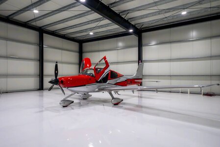 Private jet aircraft inside a modern hangar, sleek red and silver, high-tech aviation environment.
