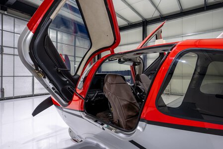 Interior view of a helicopter cockpit with open door, pilot seats, and advanced controls.