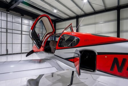 An image of a sleek racing airplane cockpit in a spacious indoor facility, showcasing advanced aerodynamics and vibrant red, silver, and black colors.