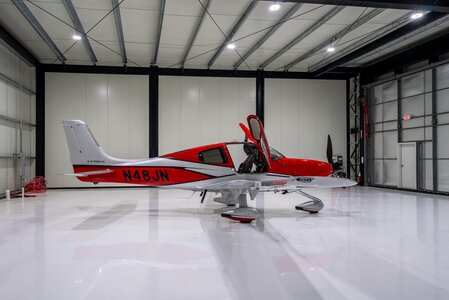 Red and white Zippy sport aircraft displayed inside spacious storage hangar with reflective polished floor.