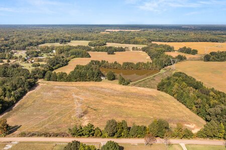Aerial view of open land with power lines, pond, and surrounding trees, ideal for development or farming.