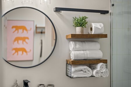 Reflective round mirror, white towels, potted plant, and toilet paper roll in stylish bathroom setup.