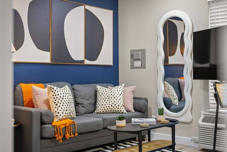 Contemporary living room featuring abstract art, patterned cushions, and a decorative white mirror.