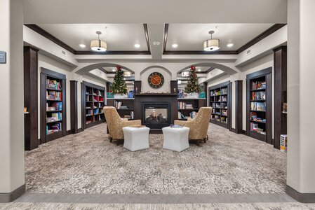 Elegant library with Christmas trees, bookshelves, and a warm fireplace for a festive ambiance.